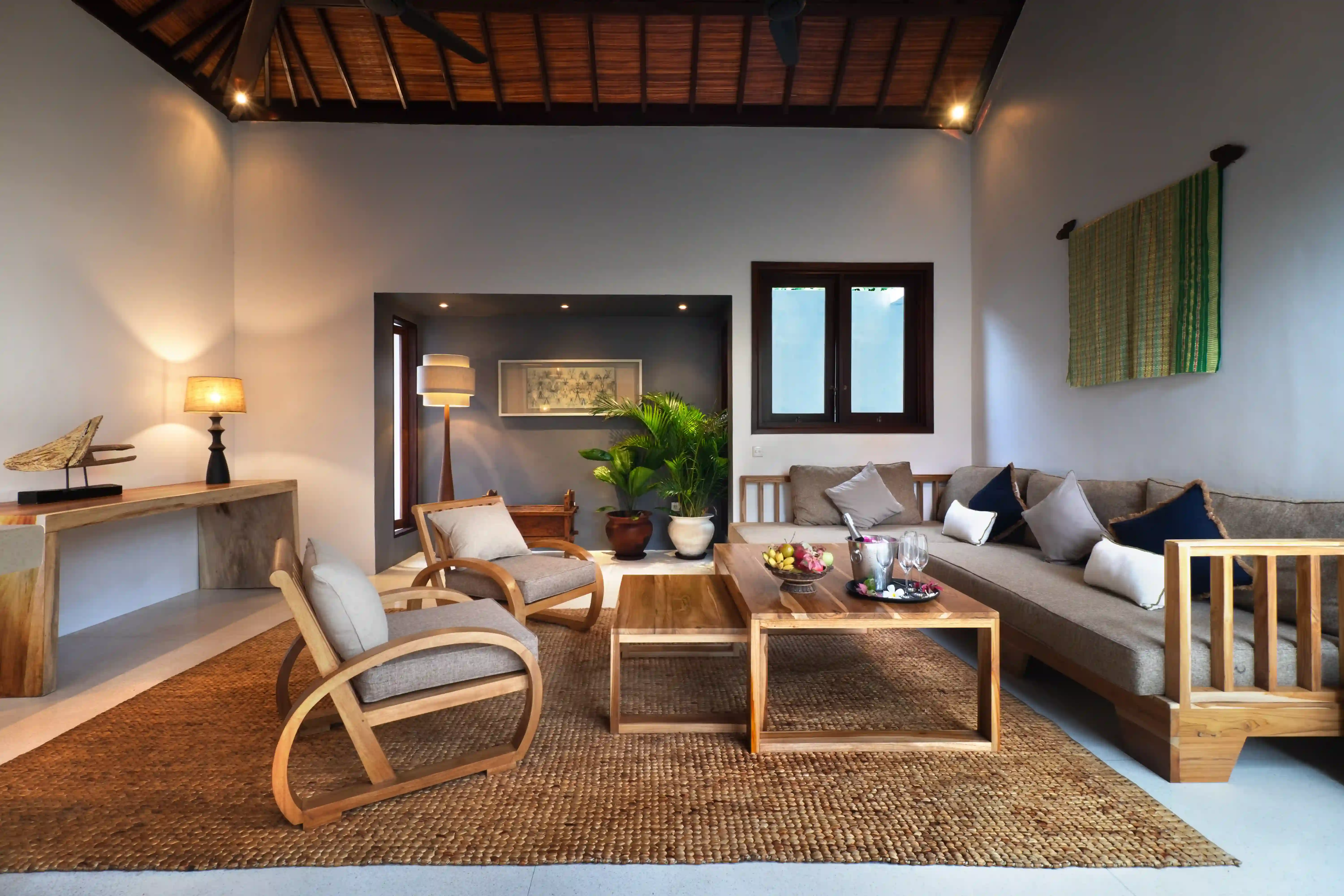 Open doorway view into the 2 Bedroom Pool Villa, showing a stylish wooden chair and modern floor lamp, with a stone accent wall outside hover