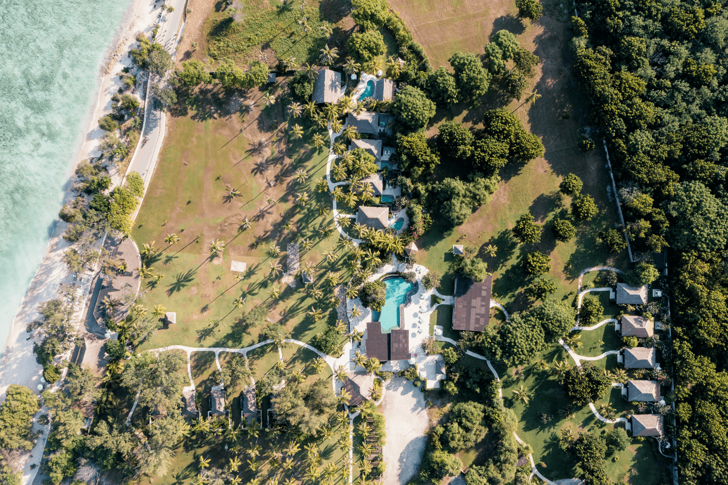 Panoramic view of Pondok Santi Estate on Gili Trawangan, showcasing pool, villas, coconut trees, expansive grounds, and beach.