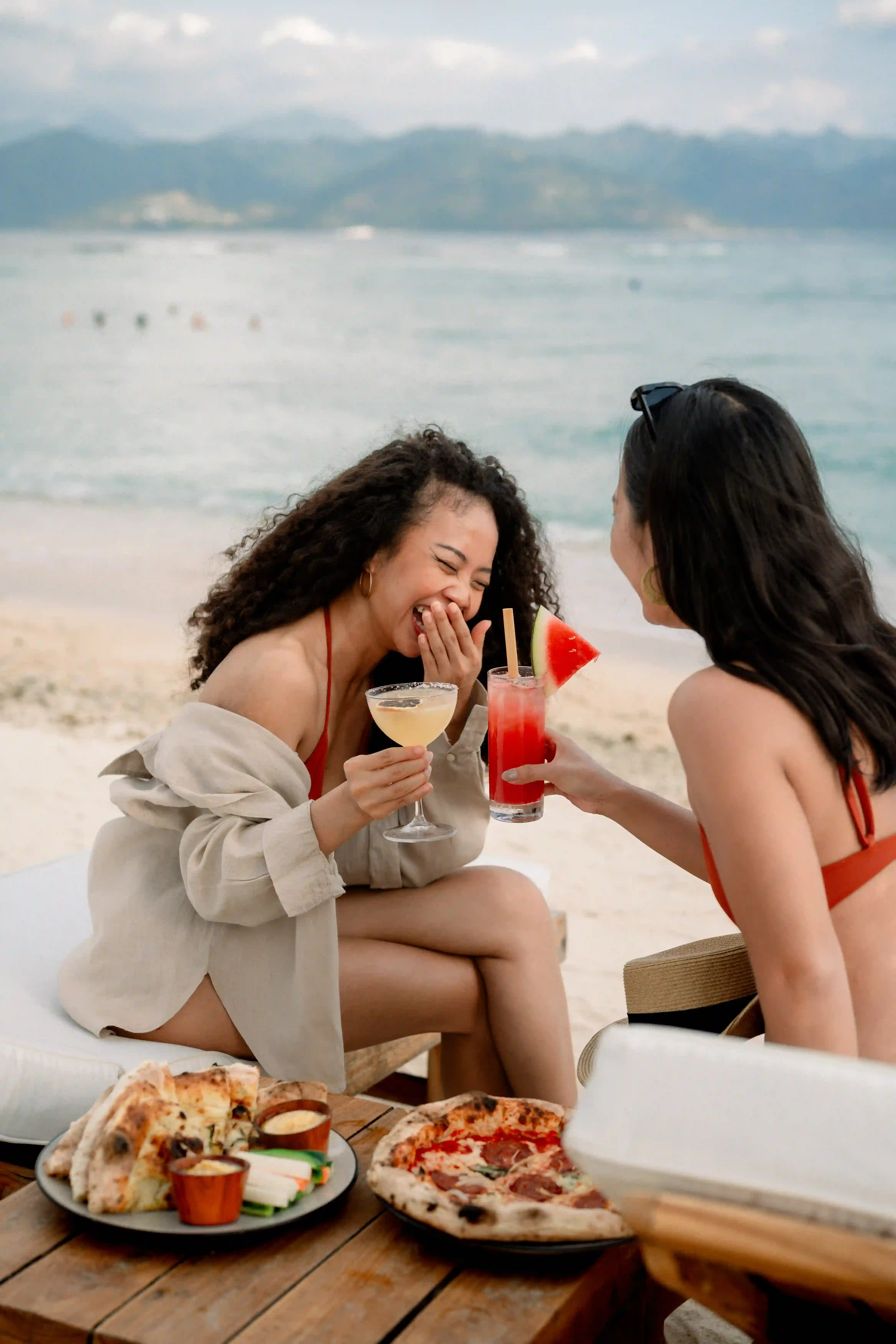 A hand wearing a gold bracelet holding an orange cocktail with ice and a garnish, resting on a wooden bar surface during Happy Hour hover