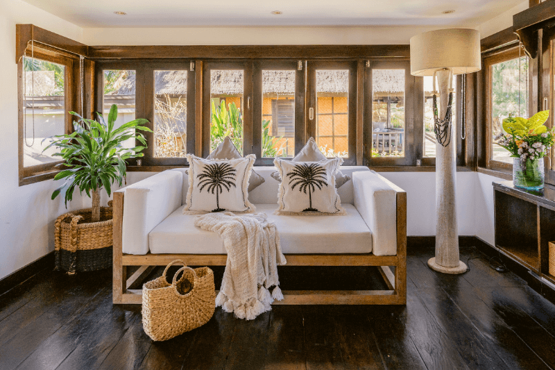 Sofa and beautiful decorations like pillows and plants inside the Palm View Bungalow at Pondok Santi Estate, Gili Trawangan, with large windows allowing natural light.