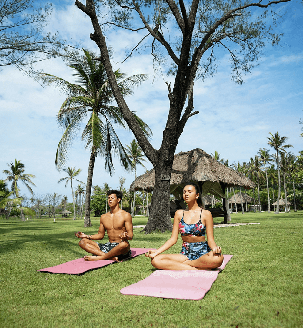 A couple practicing yoga surrounded by coconut trees and lush vegetation at Pondok Santi Estate, Gili Trawangan.
