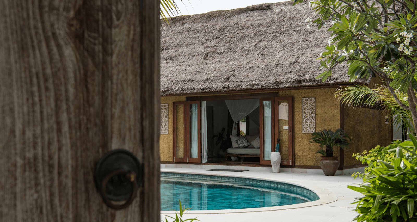 Entrance view of deluxe private pool villa with Balinese entry door, private pool in foreground, and luxurious villa in background.