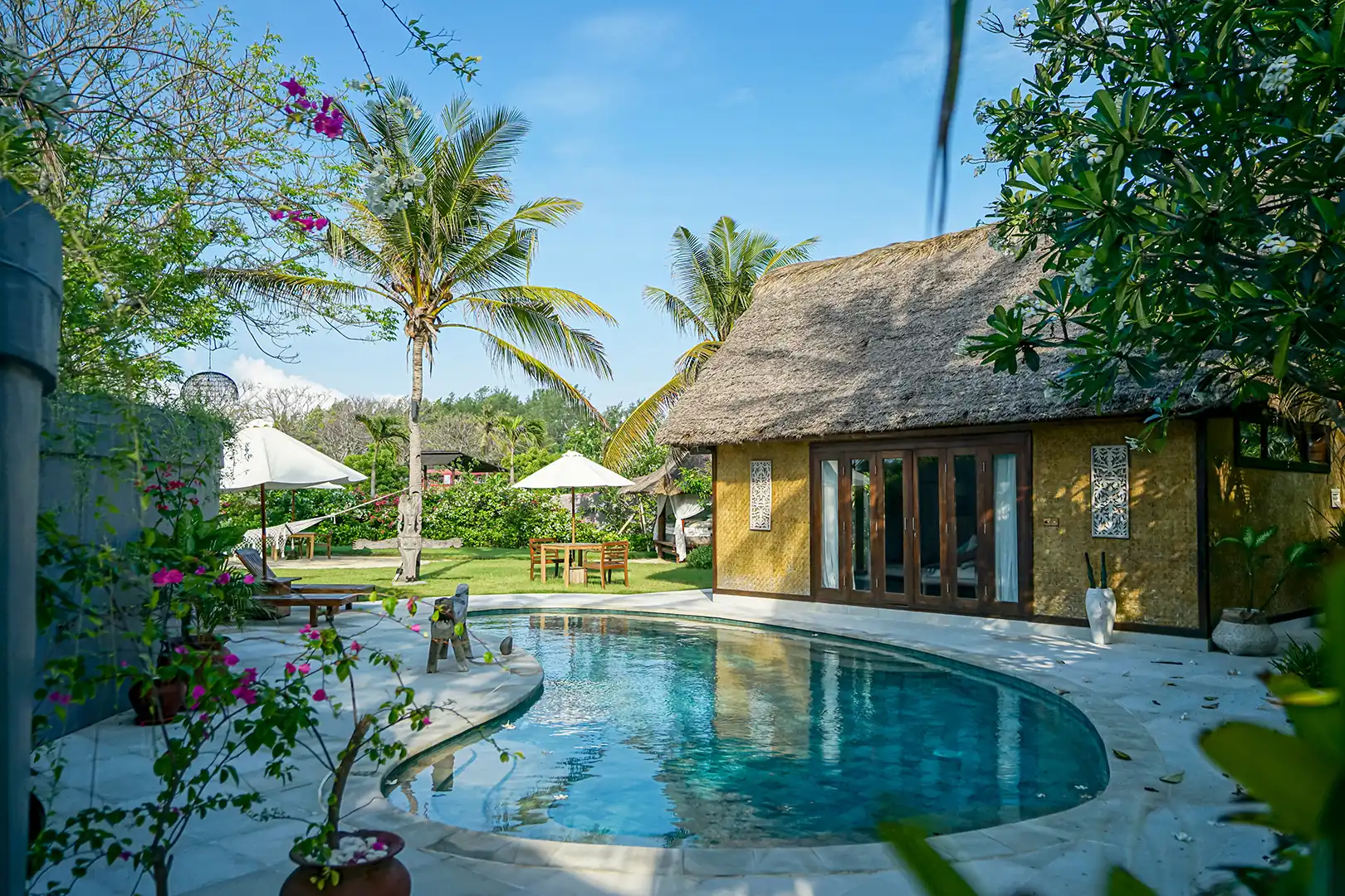 Exterior view of the Deluxe Private Pool Villa, showcasing the private lagoon-shaped pool, thatched-roof bungalow, and white stone sun terrace
