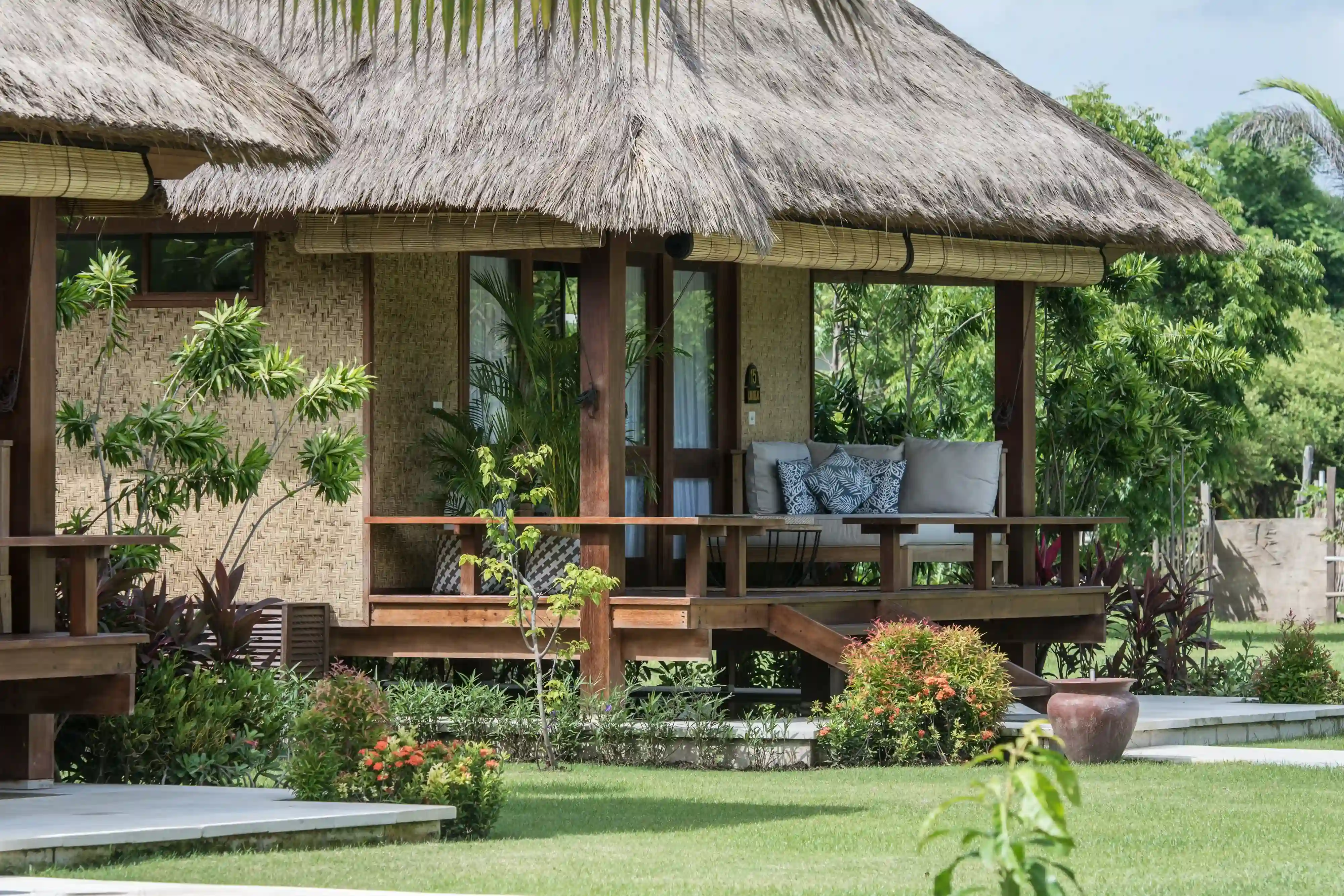 Exterior view of the Garden View Villa, showing the thatched roof, woven walls, and covered wooden terrace with a seating area