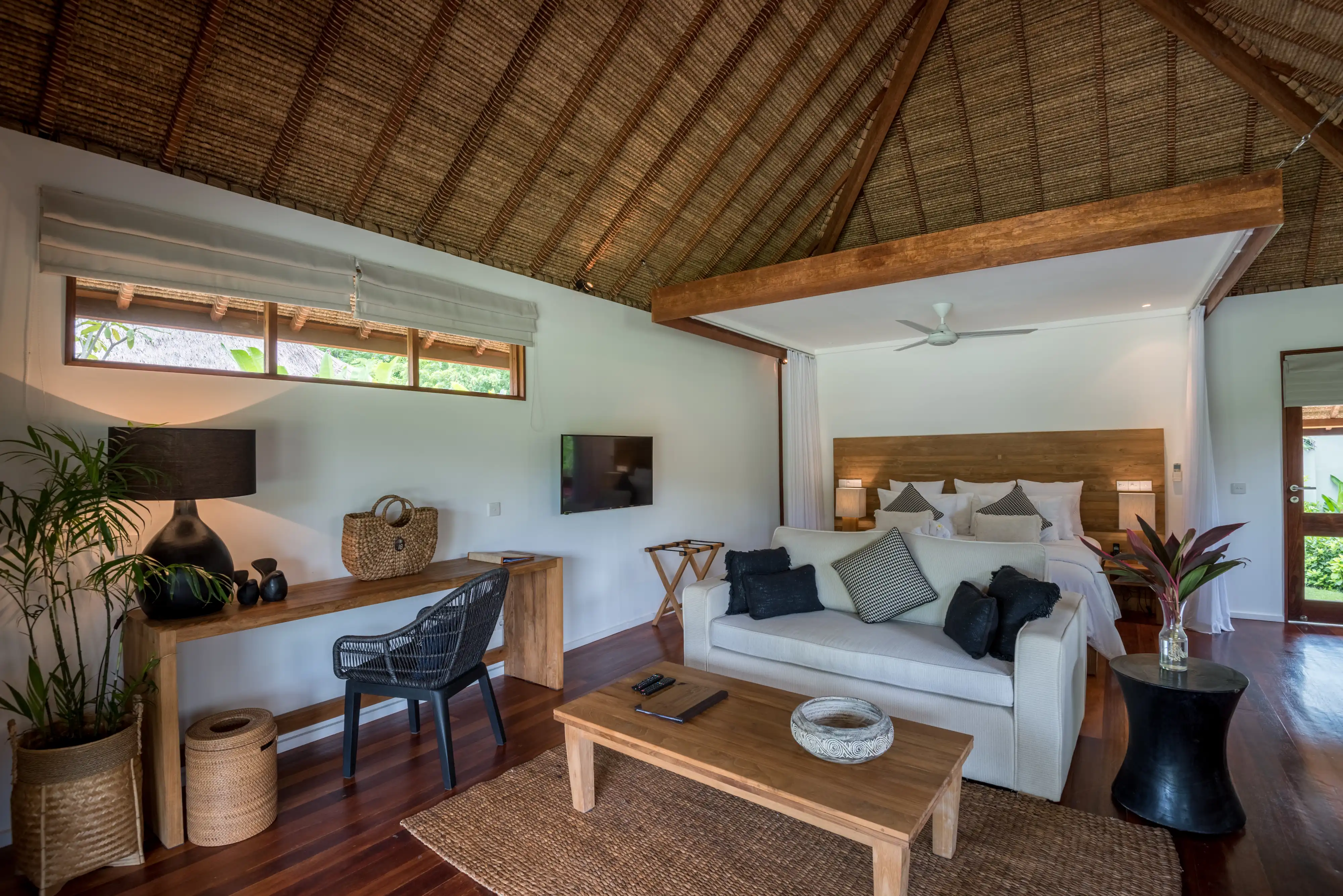 Exterior view of the Garden View Villa, showing the thatched roof, woven walls, and covered wooden terrace with a seating area hover