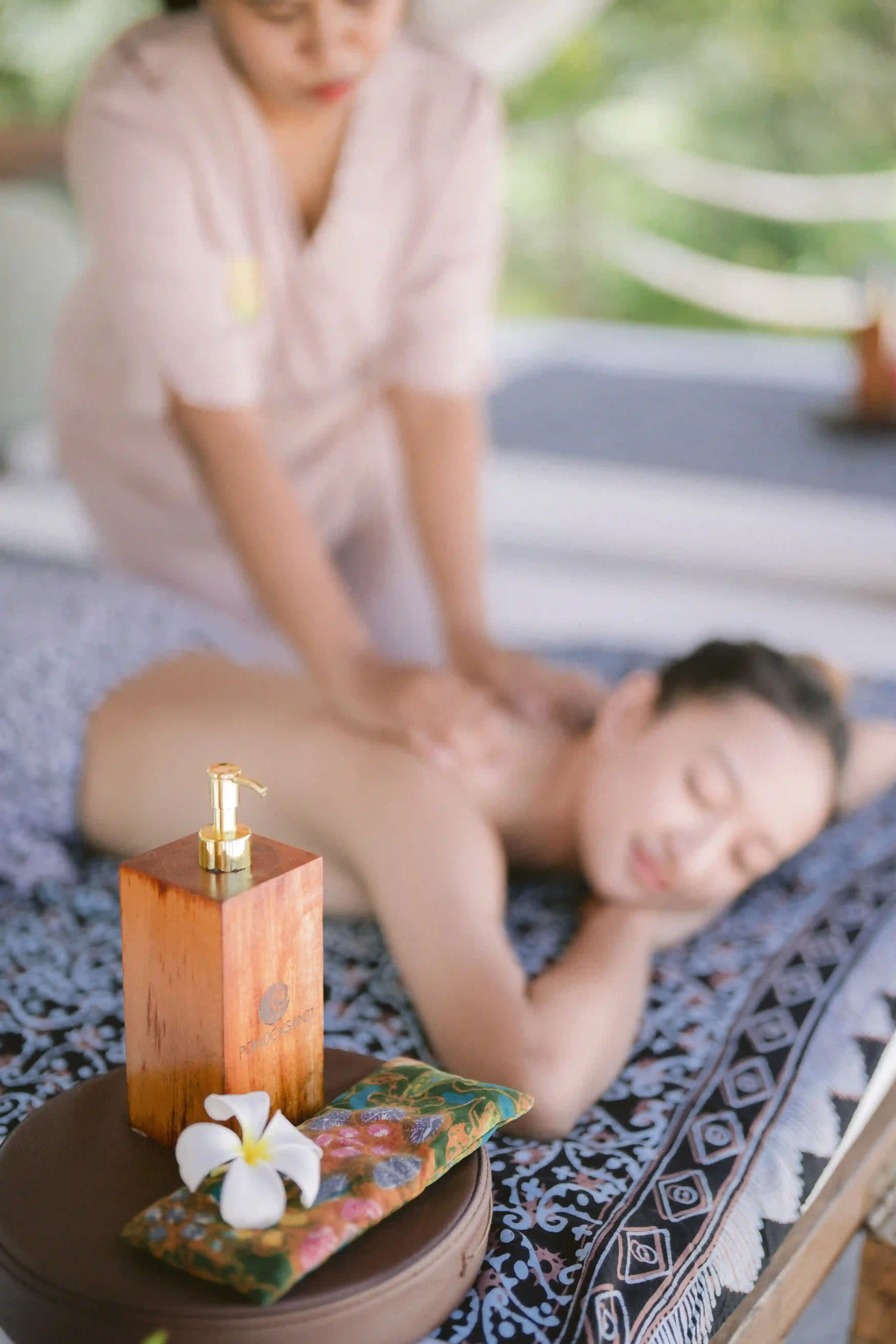 A guest receiving an in-room spa massage under a sheer white canopy on an outdoor daybed, performed by a professionally trained therapist hover