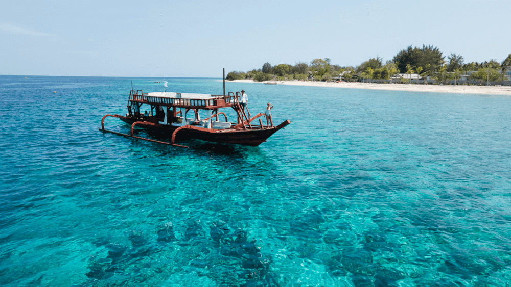 Pondok Santi's Princess Margaux, a traditional hand-built outrigger boat, sailing through crystal-clear waters.