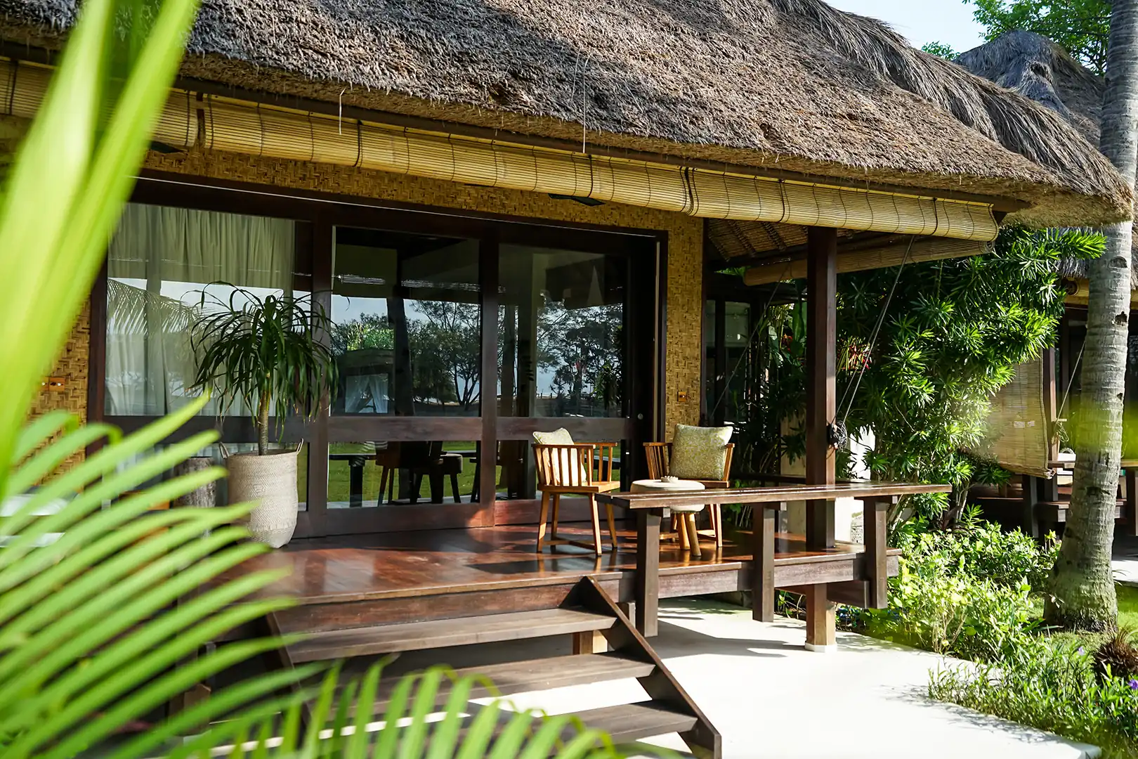Covered wooden terrace of the Ocean Private Pool Villa, with a small dining or seating area and sliding glass doors leading into the bungalow