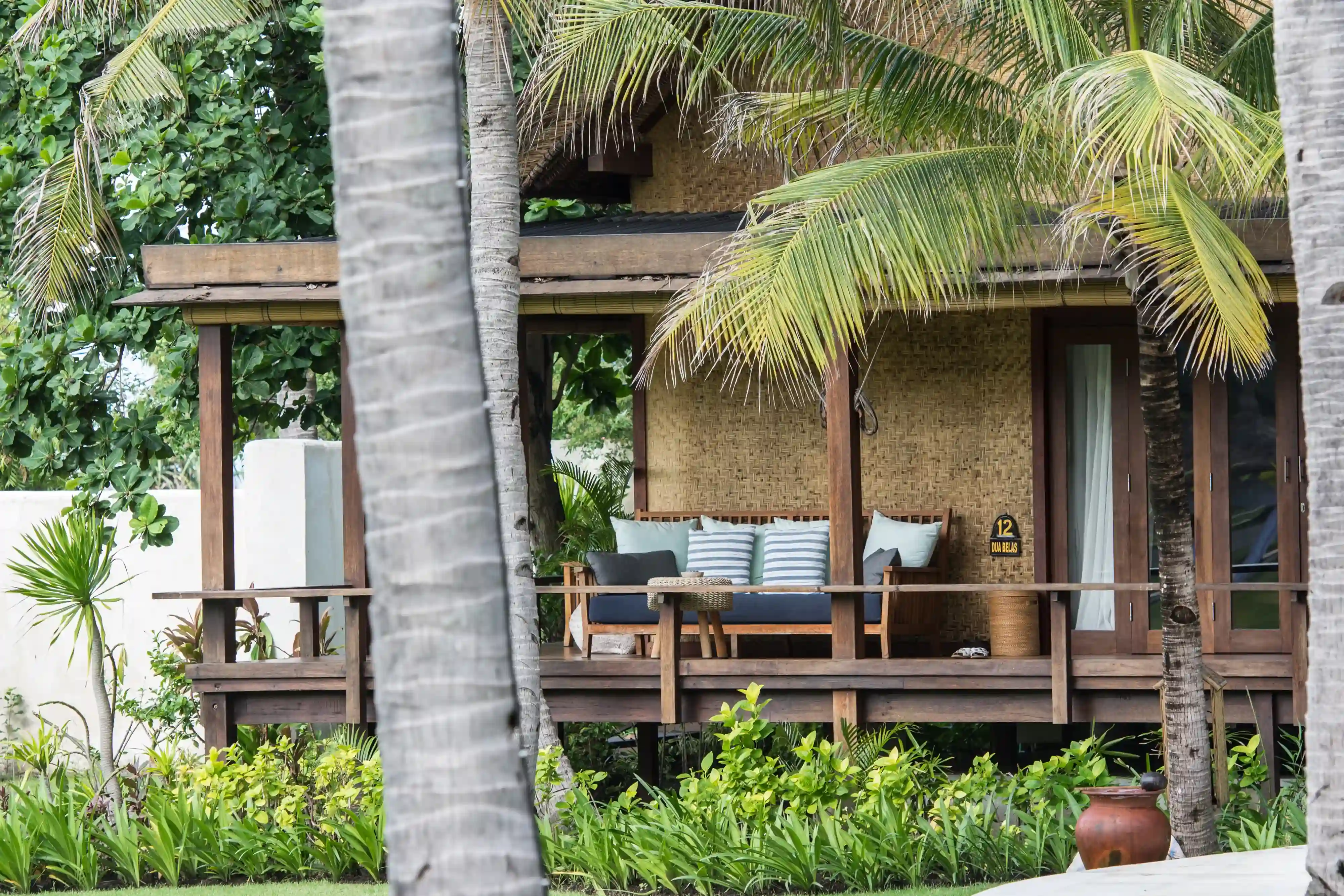 Exterior view of the Ocean View Villa's private wooden terrace with comfortable outdoor seating, seen framed by palm trees