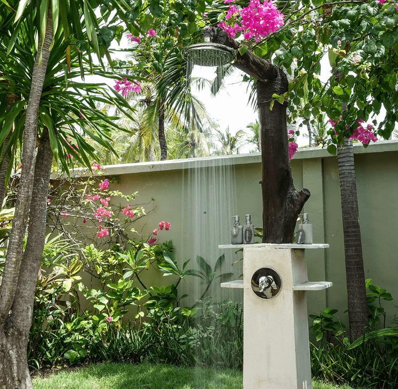 Outdoor shower of a Palm View Bungalow at Pondok Santi Estate, Gili Trawangan, surrounded by beautiful plants and flowers.
