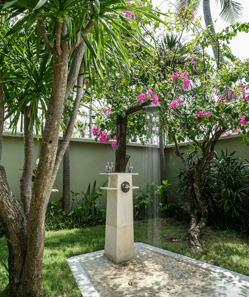 Outdoor shower at Beachside Bungalow, Pondok Santi Estate, Gili Trawangan, surrounded by beautiful trees, plants, and flowers.