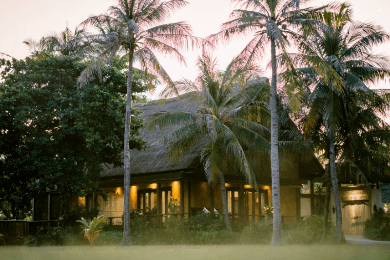Ocean View Villa at Pondok Santi Estate, Gili Trawangan, glowing in evening light amidst lush greenery and trees.