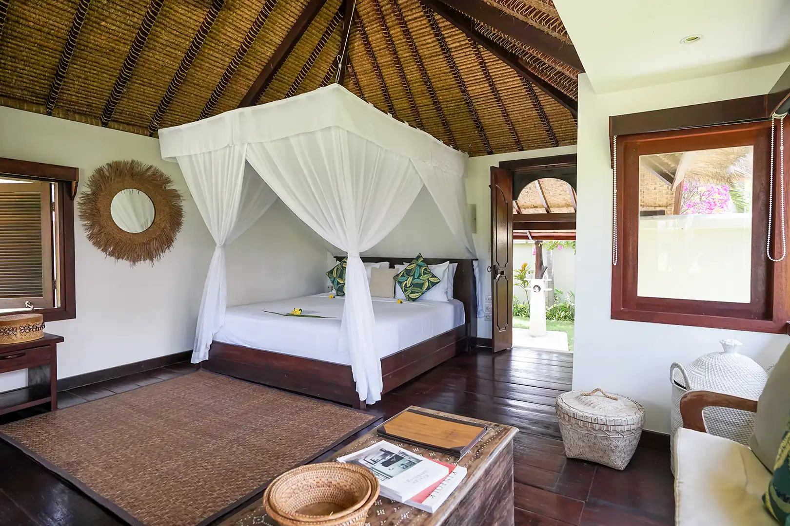 Exterior view of the Palm View Bungalow, showing the thatched roof, private wooden terrace, and palm trees surrounding the building hover