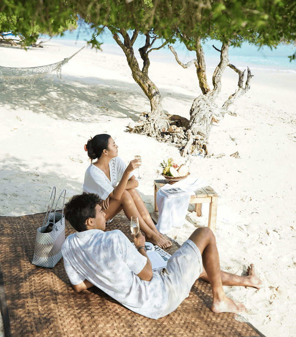 Couple enjoying a beach picnic with food and champagne at Pondok Santi Estate, Gili Trawangan.