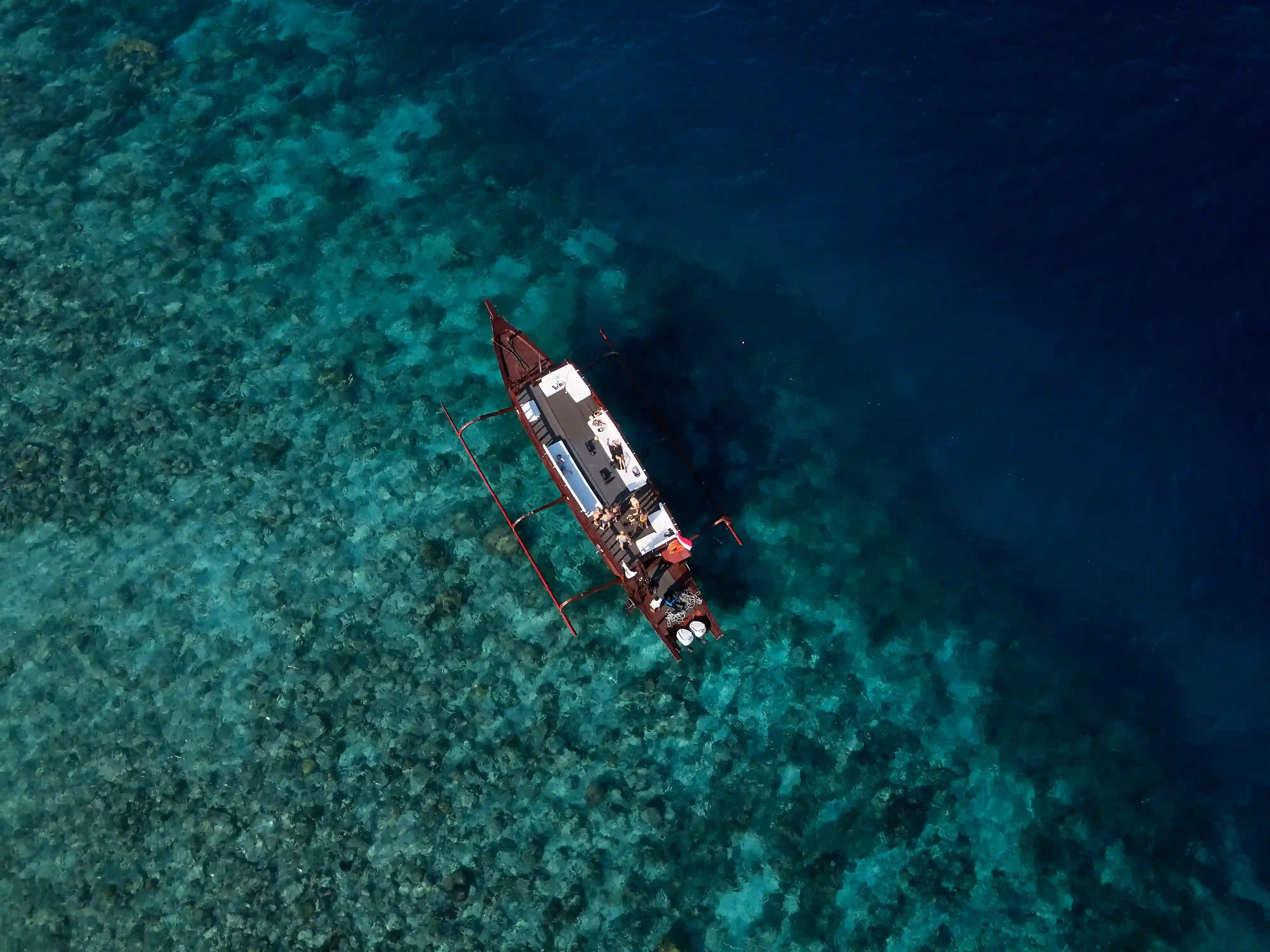 Aerial drone view of the traditional wooden outrigger Princess Margaux floating over clear turquoise reef waters near Gili Trawangan
