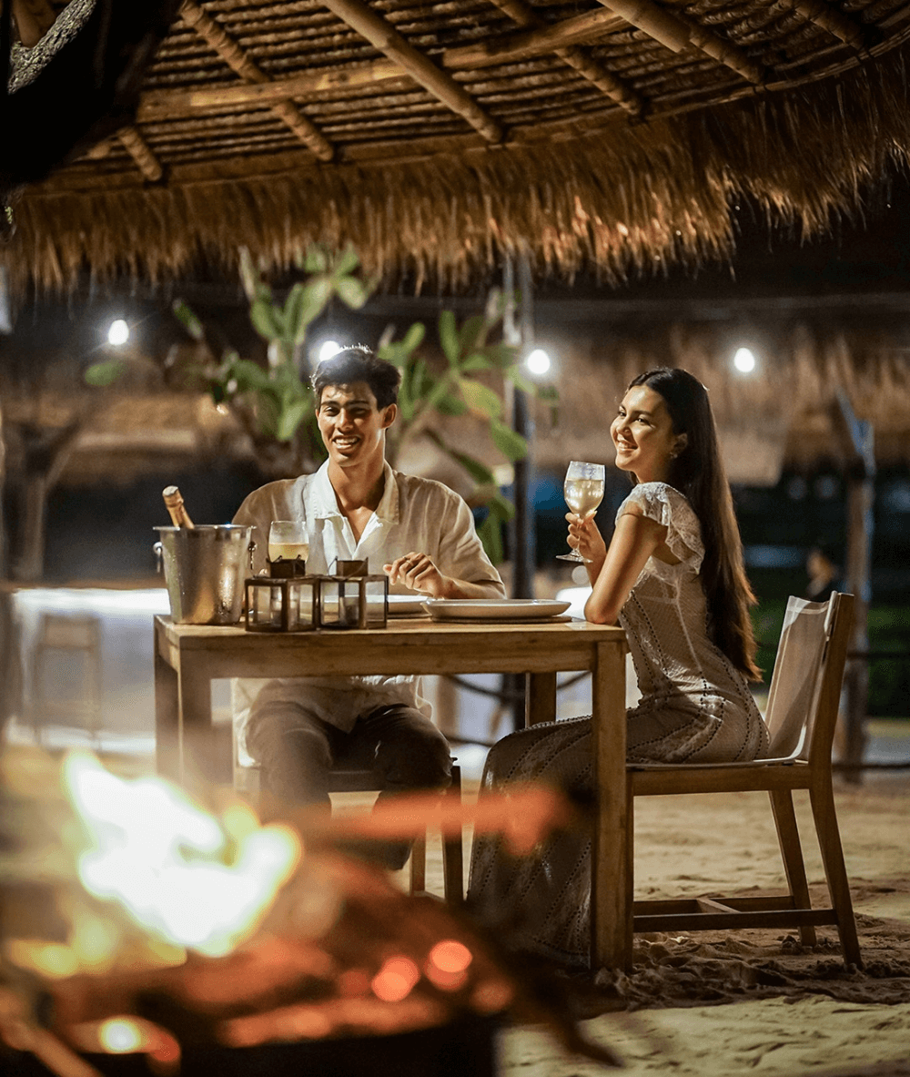 A romantic dinner at Santi Beach, Pondok Santi Estate, with a couple enjoying an evening by the beach.