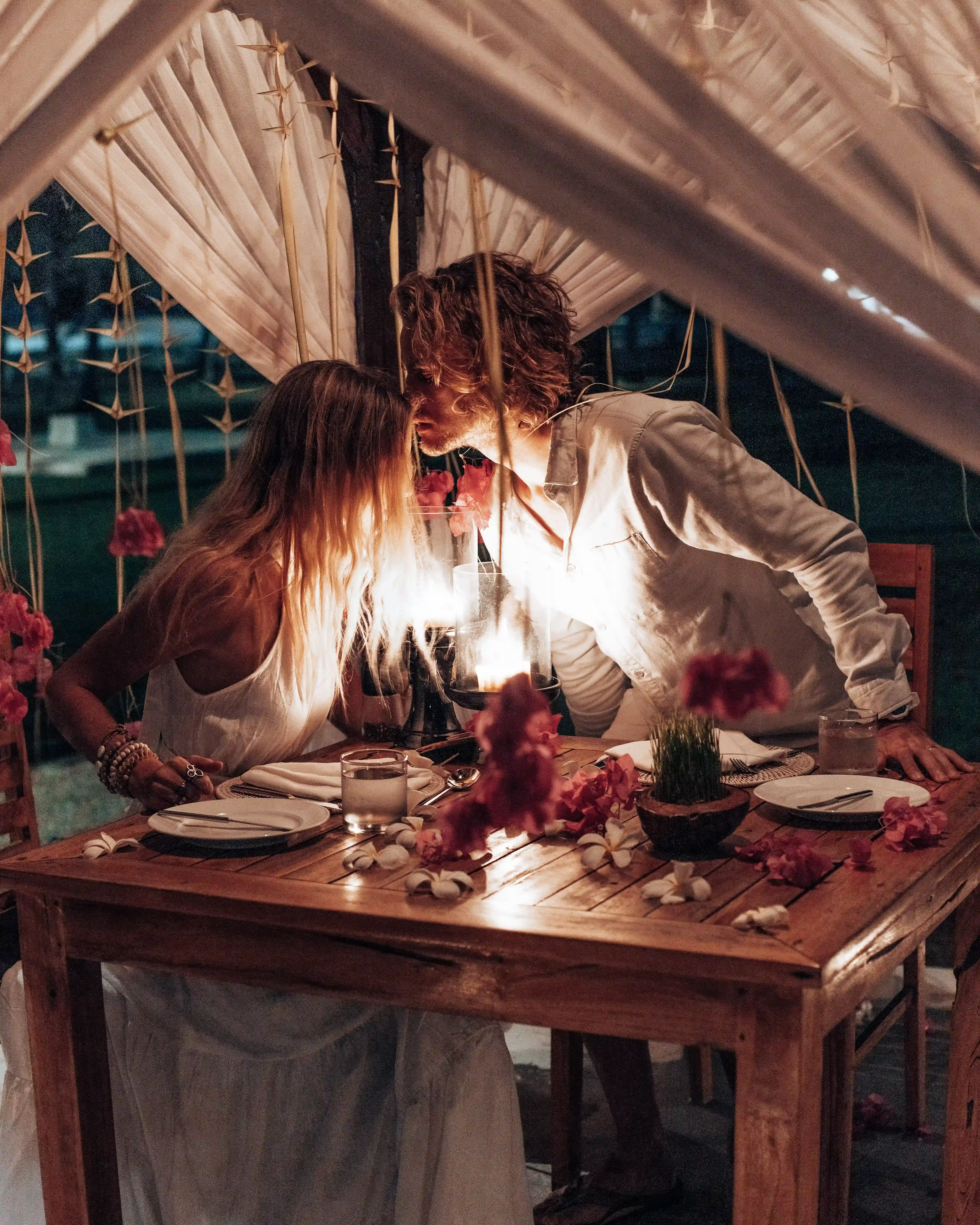 A couple shares a Romantic Dinner under a mosquito net canopy, illuminated by candlelight and decorated with flowers