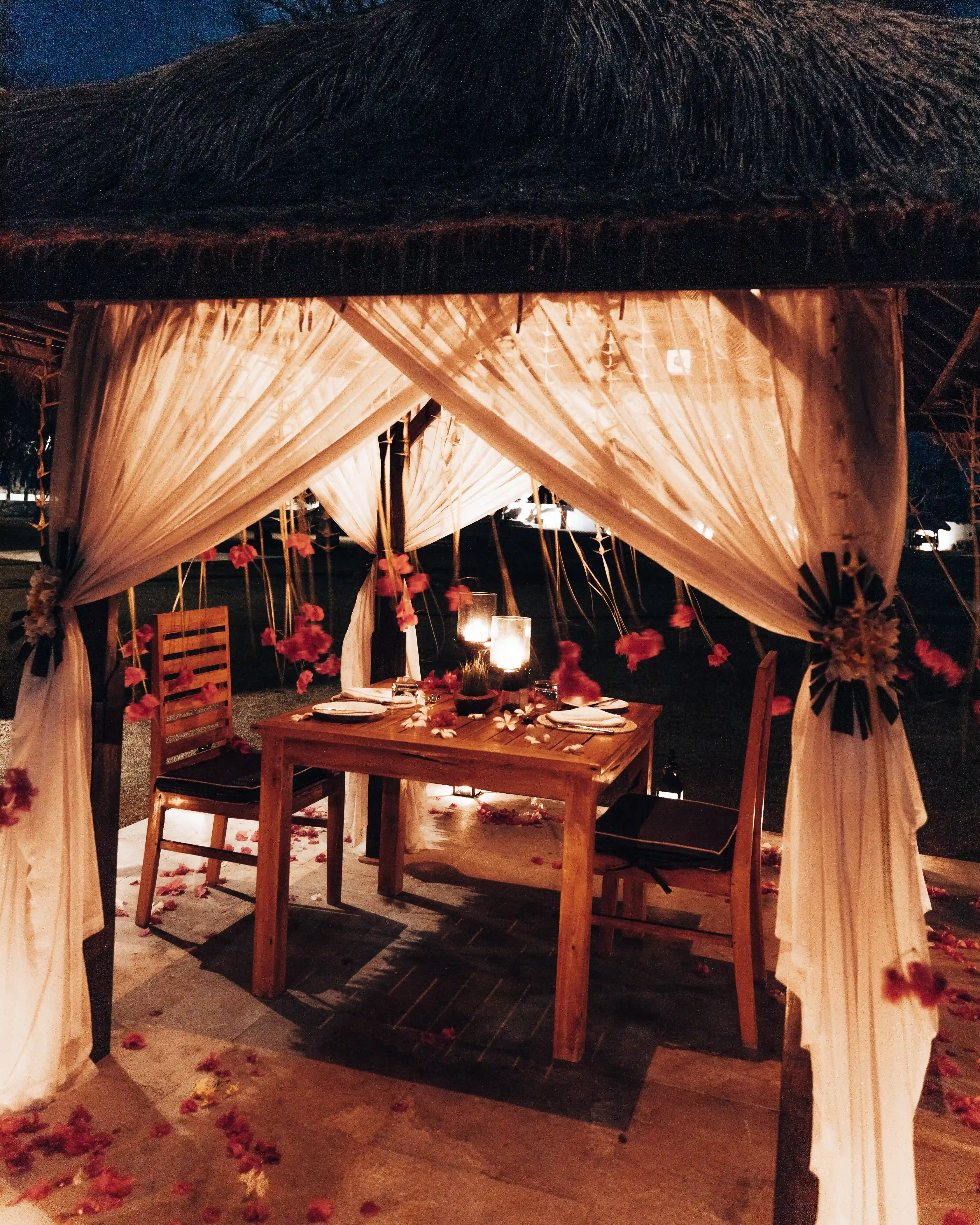 A couple shares a Romantic Dinner under a mosquito net canopy, illuminated by candlelight and decorated with flowers hover